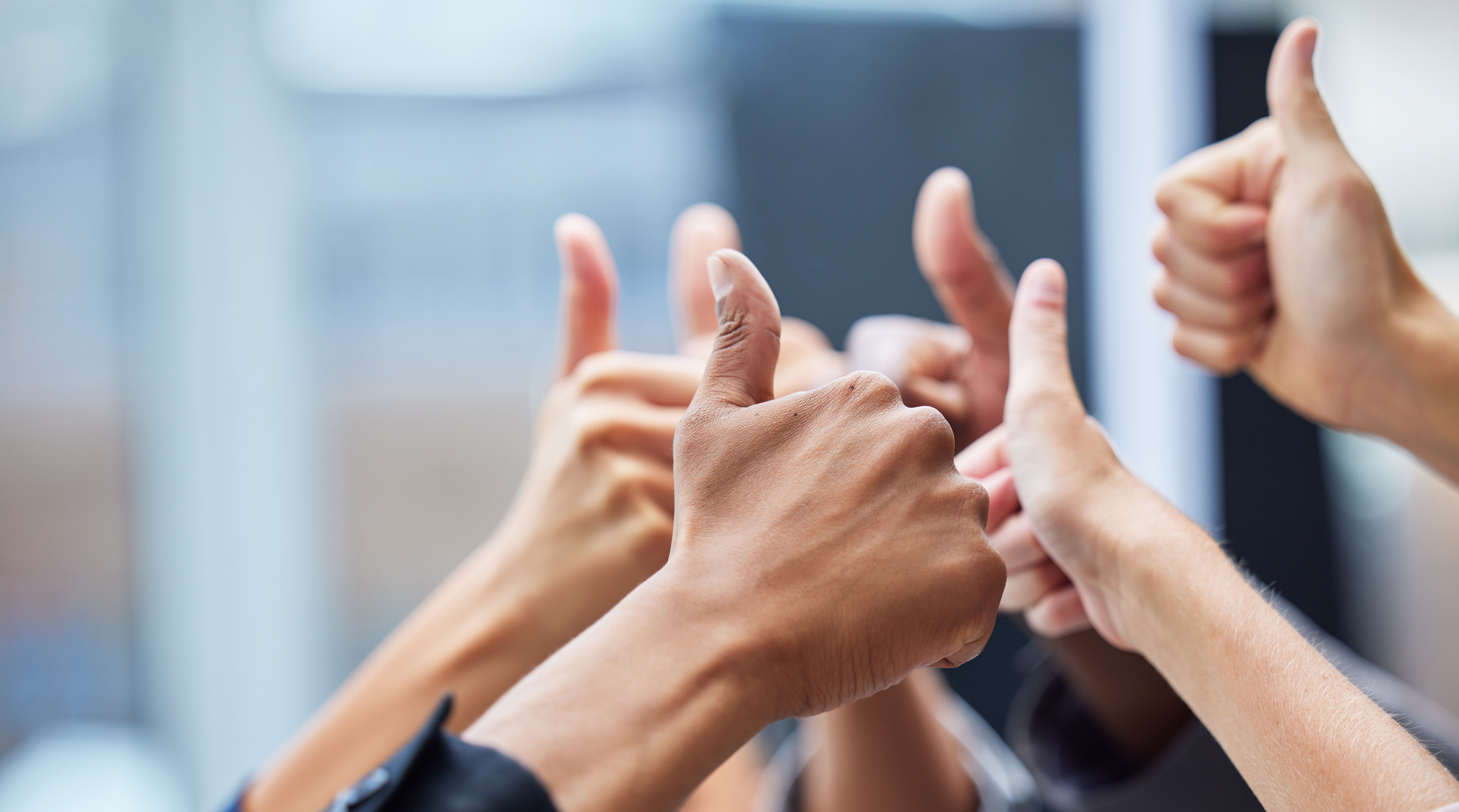 Shot of a group of coworkers with their arms raised in the thumbs up gesture